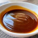 Close-up of thick, glossy homemade brown gravy in a white dipping bowl, showing whisk marks.
