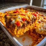A serving of cheesy Dorito Casserole being lifted from a white baking dish, showing ground meat and melted cheese.