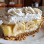 A perfect slice of banana cream pie featuring a graham cracker crust, vanilla custard, sliced bananas, and topped with whipped cream.