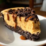A rich slice of peanut butter pie with a dark chocolate crust, topped with crushed cookies and caramel sauce.