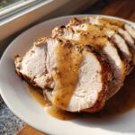 Slices of juicy instant pot turkey breast covered in savory brown gravy, seasoned with herbs.
