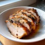 Close-up of four thick slices of juicy slow cooker turkey breast, seasoned with herbs, resting in a white bowl.