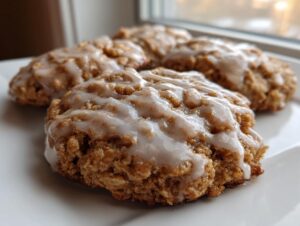 Close-up of soft iced oatmeal cookies stacked on a white plate, featuring a thick vanilla glaze.