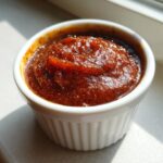 Close-up of rich, dark brown spiced pear butter served in a small, white, fluted ramekin.