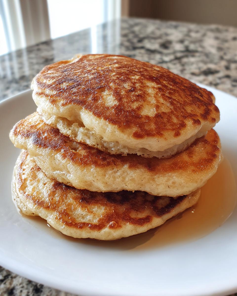 A stack of three golden-brown banana oatmeal pancakes drizzled with syrup on a white plate.