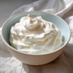 A close-up of thick, perfectly whipped white royal icing recipe mixture in a light blue bowl.
