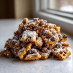 A close-up mound of crunchy toffee chex mix recipe pieces dusted heavily with white powdered sugar.