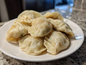 A close-up of several freshly steamed Traditional Chinese Dumplings piled on a white plate.