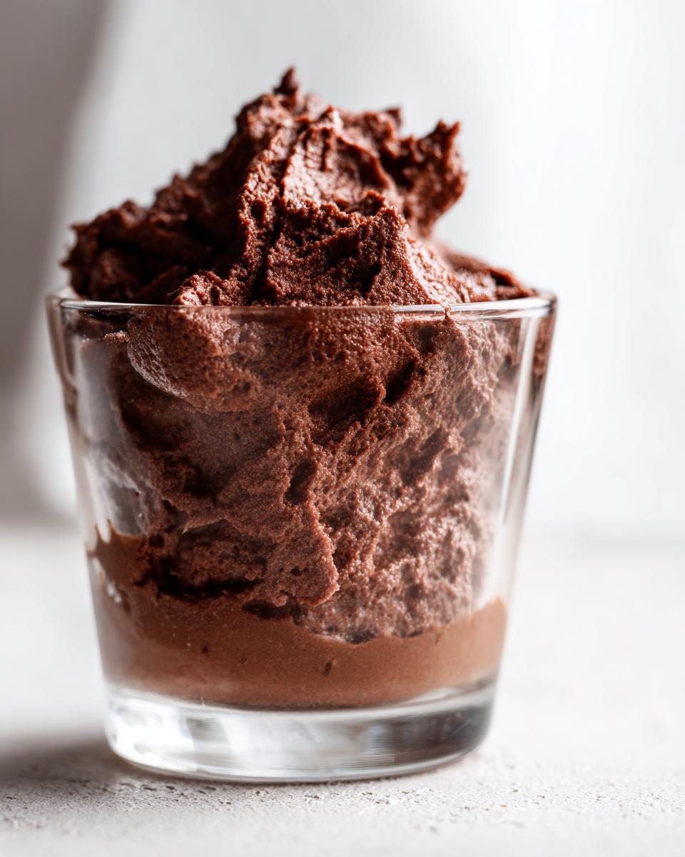 Close-up of airy, dark brown chocolate mousse served in a small clear glass.