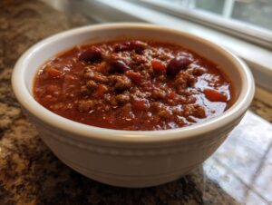 A close-up of a white bowl filled with rich, savory chili featuring ground meat and kidney beans.