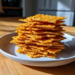 A tall stack of crispy, golden-orange 4-ingredient cheese crackers piled high on a light gray plate.