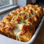 Close-up of hot, pull-apart cheese bread with melted mozzarella and herbs in a white baking dish.