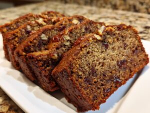 Four moist slices of amazing date nut bread, studded with dates and pecans, served on a white plate.