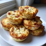 A stack of six golden brown, savory egg bites topped with bacon bits, ready for breakfast.