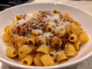 A close-up shot of a serving of amazing french onion pasta topped with caramelized onions and grated Parmesan cheese.
