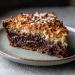 Close-up of a rich slice of german chocolate pie showing a dark chocolate layer and toasted coconut topping.