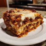 A thick, hearty slice of homemade lasagna showing layers of pasta, rich meat sauce, and melted cheese.