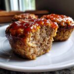 Close-up of a mini meatloaf with a bite taken out, showing the moist interior and sweet glaze topping.