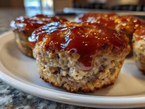 A close-up shot of a perfectly cooked mini meatloaf topped with a thick, shiny glaze, ready to eat.