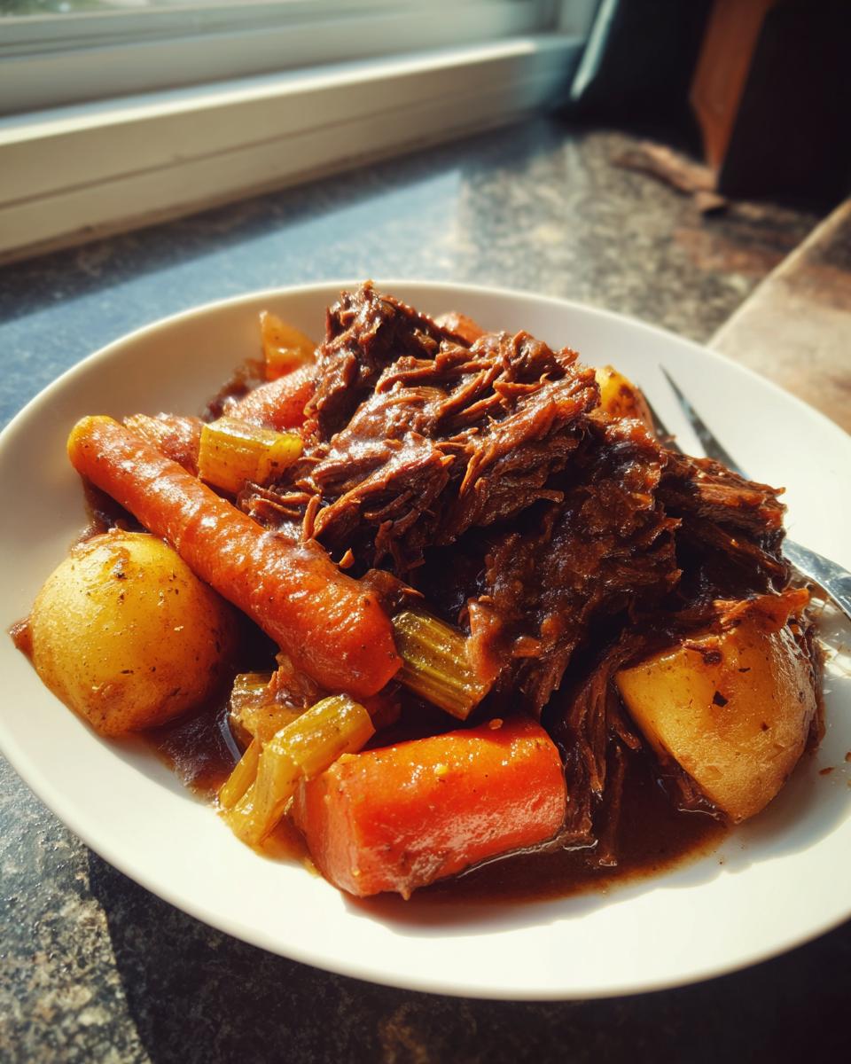 A serving of tender, shredded pot roast served with large chunks of carrots and potatoes in rich gravy.
