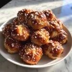 A pile of golden brown, shiny soft pretzel bites sprinkled generously with coarse pretzel salt.