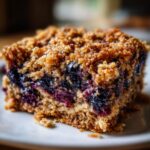 Close-up of a square slice of blueberry baked oatmeal with a thick, crunchy brown sugar crumble topping.