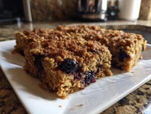 Two golden brown squares of blueberry baked oatmeal with a crumbly topping served on a white plate.