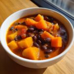 Close-up of a white bowl filled with rich, orange butternut squash chili and black beans.