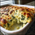 A scoop of hot, cheesy spinach artichoke dip being lifted from a white baking dish, showing melted cheese strings.