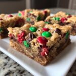 Close-up of a chewy, thick christmas cookie bars square topped with red and green M&Ms and chocolate chips.