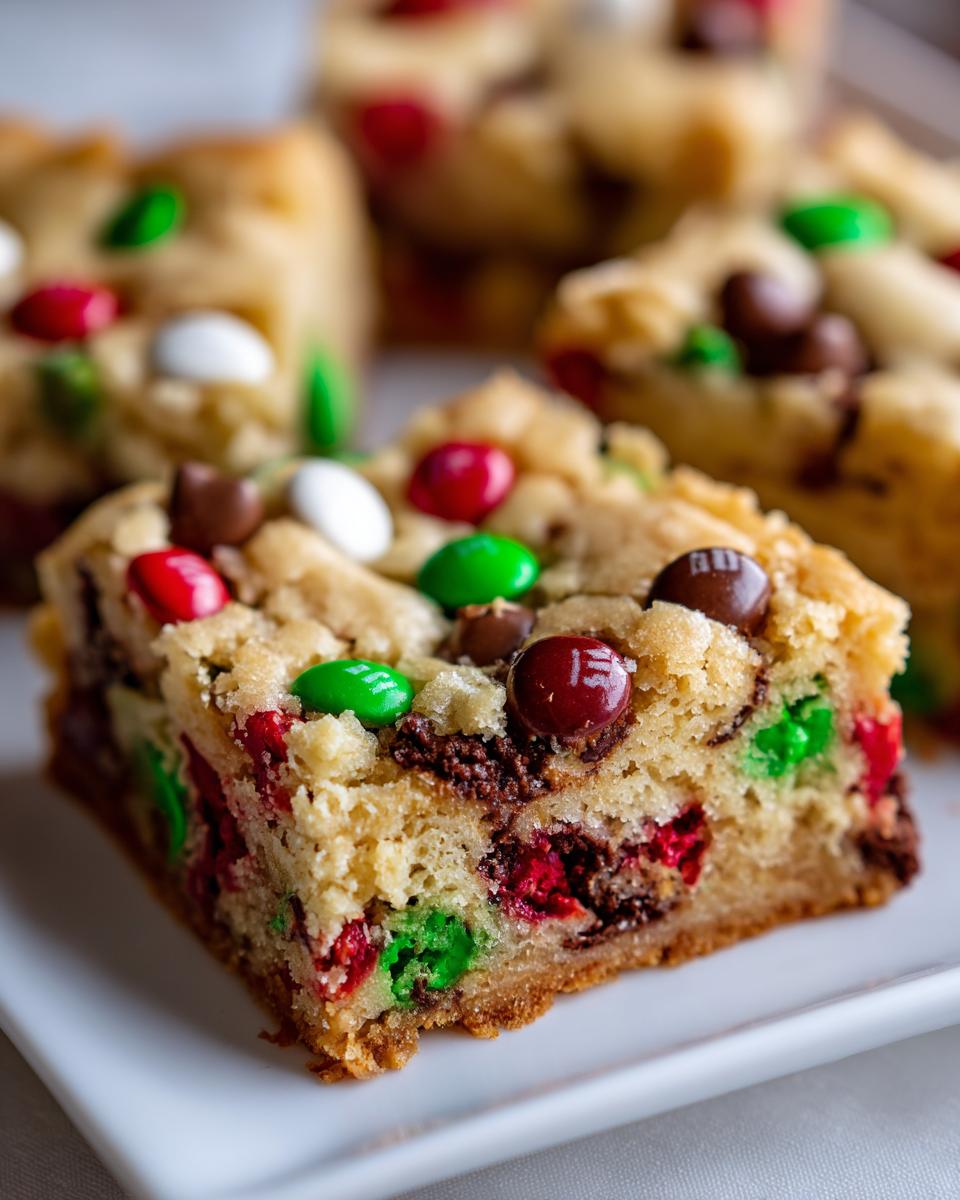 A close-up view of a thick, chewy slice of christmas cookie bars studded with red, green, and white M&M candies.