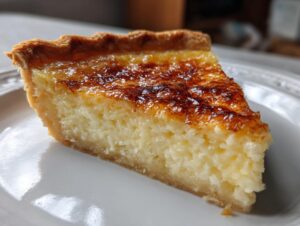A close-up of a slice of classic buttermilk pie showing the creamy filling and deeply caramelized top crust.