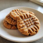 Close-up of three classic peanut butter cookies with fork crosshatch marks, sprinkled with sugar.