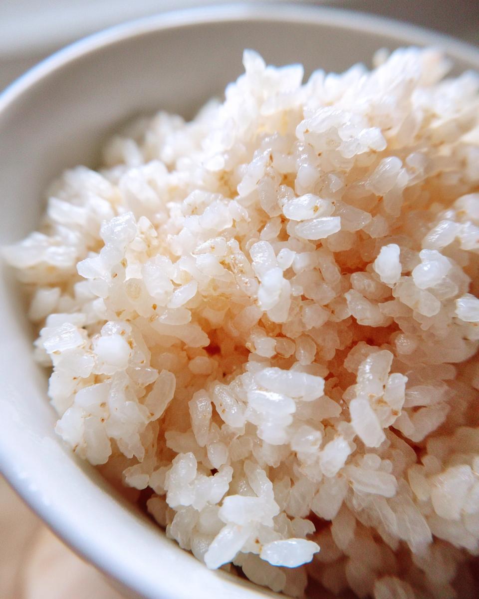 Close-up of perfectly cooked, slightly sticky sushi rice grains in a white bowl, ready for rolling.