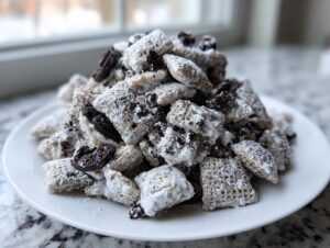 A close-up photo of a large pile of cookies and cream puppy chow coated in white powder, served on a white plate.
