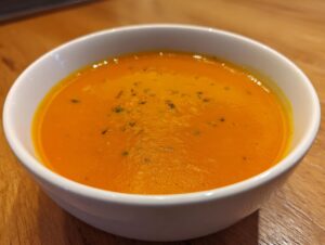 A close-up of a bowl of vibrant orange, creamy butternut squash soup garnished with herbs.