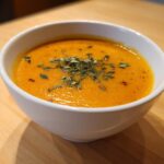 A close-up of a bowl of creamy butternut squash soup, garnished with fresh herbs.
