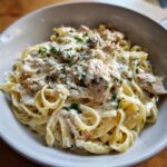 Close-up of a bowl filled with creamy chicken alfredo pasta, topped with grated Parmesan and fresh parsley.