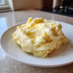 A generous scoop of fluffy, creamy mashed potatoes topped with melting butter on a white plate.