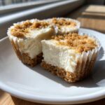 A close-up of two creamy mini cheesecake portions on a white plate, showing the graham cracker crust and crumb topping.