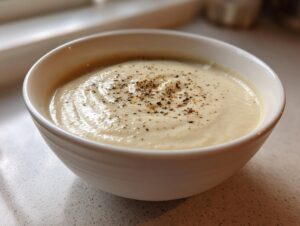 Close-up of a creamy bowl of roasted cauliflower soup garnished with freshly cracked black pepper.