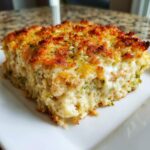 A close-up of a creamy, cheesy slice of vegetable casserole topped with golden brown, herbed breadcrumbs.