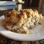 A close-up serving of moist crock pot chicken and stuffing with a golden, herbed topping on a white plate.