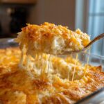 A spoonful of creamy crockpot cheesy potatoes being lifted, showing long, melted cheese strings.