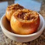 Close-up of two perfectly baked apples, cored and filled with a brown sugar and nut crumble topping.