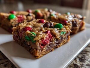 A close-up view of a gooey, chewy square of christmas cookie bars topped with red and green M&Ms.