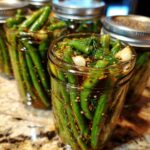 Close-up of fresh dilly beans packed tightly in canning jars with garlic cloves, dill sprigs, and spices.