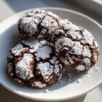 Close-up of three rich, dark chocolate crinkle cookies heavily dusted with powdered sugar.