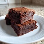A stack of three rich, fudgy date brownies with a slightly crackled top, served on a white plate.