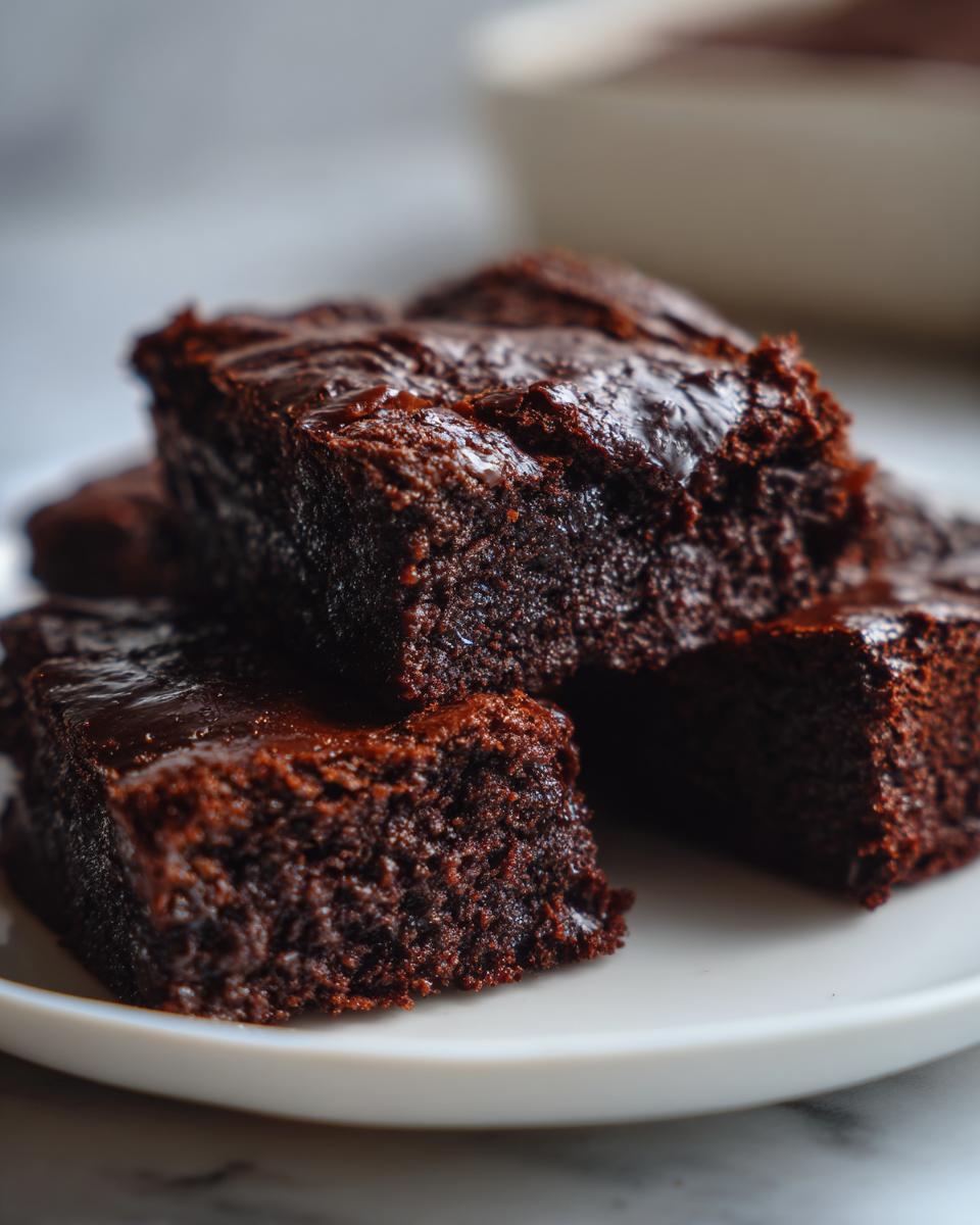 Close-up of several rich, fudgy date brownies stacked on a white plate, showing their moist texture.